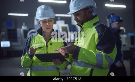 Chief Engineer und Projektmanager tragen Sicherheitswesten und Hats, verwenden Sie digitale Tablet-Computer in der modernen Fabrik, sprechen, Optimierung der Produktion Stockfoto