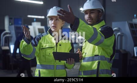 Chief Engineer und Projektmanager tragen Sicherheitswesten und Hats, verwenden Sie digitale Tablet-Computer in der modernen Fabrik, sprechen, Optimierung der Produktion Stockfoto