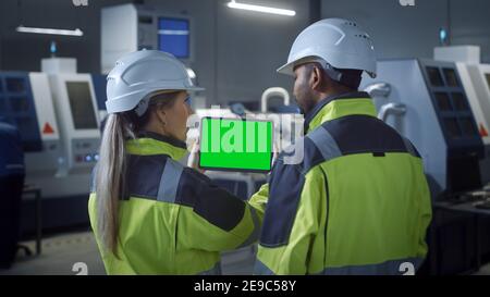 Industrie 4,0 Fabrik: Chief Engineer und Project Supervisor in Sicherheitswesten und Hüte, sprechen, verwenden Sie digitale Tablet-Computer mit grünem Bildschirm, Chroma Stockfoto