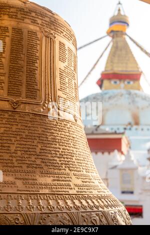 Kathmandu, Nepal - Januar 29 2021: Buddhistische Handschriften auf die goldene Glocke eingeschrieben mit Boudhanath Stupa im Hintergrund. Stockfoto