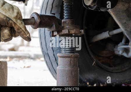 Reifenservice, Car Service Konzept. Hand in Handschuh hebt das Fahrzeug mit einem mechanischen Wagenheber an. Ersetzen eines Platten Reifens. Selektiver Fokus. Stockfoto