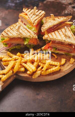 Club Sandwiches auf einem Holzbrett serviert. Mit heißen Pommes frites Stockfoto