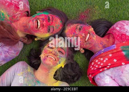 DREI JUNGE FRAUEN, DIE NACH DEM HOLI-SPIEL GLÜCKLICH AUF GRAS LIEGEN Stockfoto