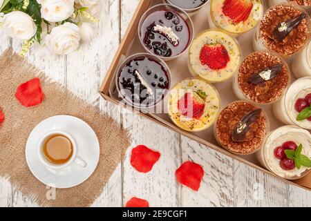 Süßes Dessert im Glas mit Keks, Beerenobst und Schlagsahne. Eine Tasse Tee, Blumen, Kuchen in einer Schachtel. Lieferung von Lebensmitteln an das Haus für Partys oder Stockfoto