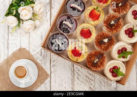 Süßes Dessert im Glas mit Keks, Beerenobst und Schlagsahne. Eine Tasse Tee, Blumen, Kuchen in einer Schachtel. Lieferung von Lebensmitteln an das Haus für Partys oder Stockfoto