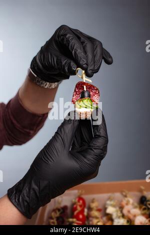 CANape, Hände in schwarzen Handschuhen halten eine schöne Canape auf einer Kappe. Catering, Snacks, schönes Essen. Studio-Foto. Stockfoto