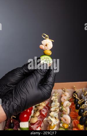 CANape, Hände in schwarzen Handschuhen halten eine schöne Canape auf einer Kappe. Catering, Snacks, schönes Essen. Studio-Foto. Stockfoto