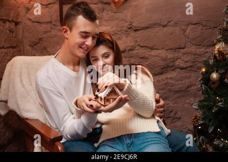 Eine junge Familie träumt von ihrem eigenen Zuhause, Hypothek, Darlehen. Ein Mädchen und ein Kerl in einem Neujahrsfotostudio. Weihnachtsträume. Junge Menschen halten ein h an Stockfoto