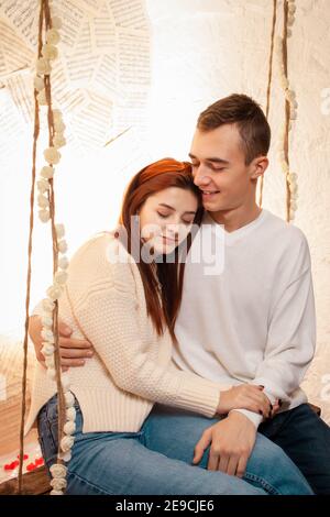 Ein junges verliebes Paar sitzt auf einer Schaukel. Posiert für Models in einem Fotostudio. Der Typ und das Mädchen lieben sich, kuscheln. Stockfoto