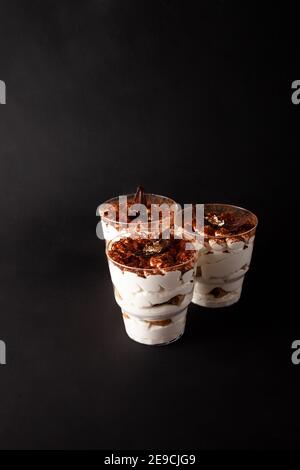 Süßes Dessert in Glas Tiramisu auf schwarzem Hintergrund in einem niedrigen Schlüssel. Leeres Leerzeichen für Text. Stockfoto