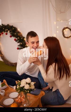 Ein junges glückliches Paar in der Liebe isst in einem Fotostudio. Der Kerl und das Mädchen sind lustig Fütterung einander. Posiert für Models in einem Studio zu Weihnachten. F Stockfoto