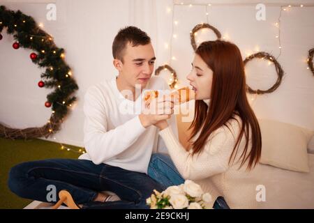 Ein junges glückliches Paar in der Liebe isst in einem Fotostudio. Der Kerl und das Mädchen sind lustig Fütterung einander. Posiert für Models in einem Studio zu Weihnachten. F Stockfoto