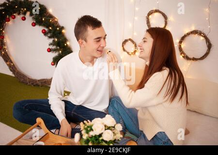 Ein junges glückliches Paar in der Liebe isst in einem Fotostudio. Der Kerl und das Mädchen sind lustig Fütterung einander. Posiert für Models in einem Studio zu Weihnachten. F Stockfoto