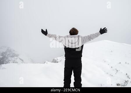 Ein Mann steht auf einem Grat mit ausgestreckten Armen Im Winter Stockfoto