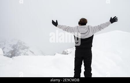 Ein Mann steht auf einem Grat mit ausgestreckten Armen Im Winter Stockfoto