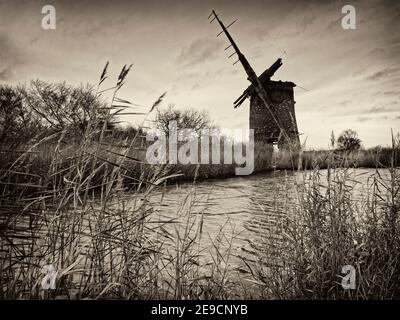 Die Überreste der Brograve Drainage Mill auf Waxham New Cut in der Nähe von Horsey, Norfolk an einem grauen Dezembertag mit sterbendem Schilf und bewölktem Himmel. Monobild... Stockfoto