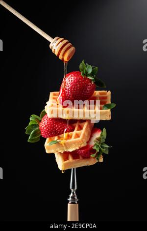 Waffeln mit Erdbeeren und Honig auf schwarzem Hintergrund. Stockfoto