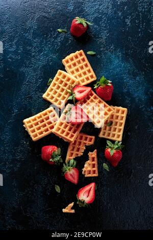 Waffeln mit frischen saftigen Erdbeeren auf dunkelblauem Hintergrund, Blick von oben. Stockfoto