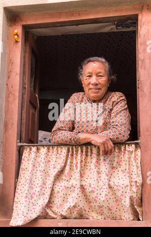 Freundliche, hochrangige nepalesische Frau im Fenster ihres Hauses in Kirtipur, Nepal Stockfoto