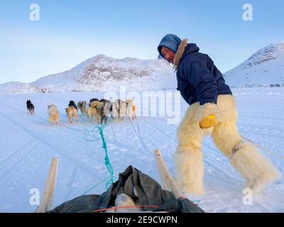 Springen auf dem Schlitten. Inuit Jäger in traditionellen Hosen und Stiefeln aus Eisbärenfell auf dem Meereis der Melville Bay bei Kullorsuaq Stockfoto