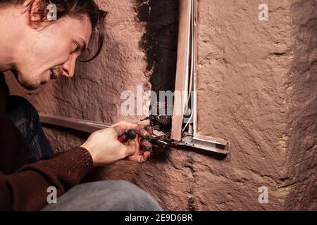 Ein Mann repariert eine verbrannte Steckdose. Kurzschluss, verbrannte