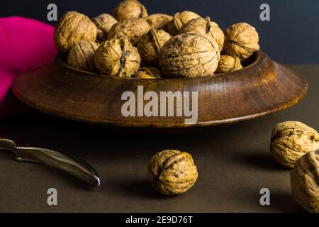 Ganze Walnüsse in einer Holzschale, Nussknacker auf der Seite, dunkler Hintergrund. Stockfoto