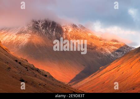 Nahaufnahme schneebedeckten Bergkette in dicken Wolken mit lebendigen roten Sonnenfarben bedeckt. Great Gable, Lake District, Großbritannien. Stockfoto