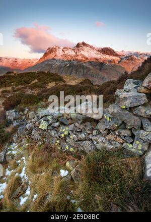 Alte ländliche Steinmauer mit Blick auf die schneebedeckten Cumbrian Berge; die Langdale Pikes als Morgensonne wirft einen rosa Glanz. Lake District, Großbritannien. Stockfoto