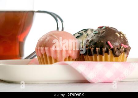 Tasse mit Tee und leckeren Mini-Cupcakes mit dunkler Schokolade, Erdbeere und weiße Schokolade auf Holztisch und weißem Hintergrund bedeckt. Stockfoto