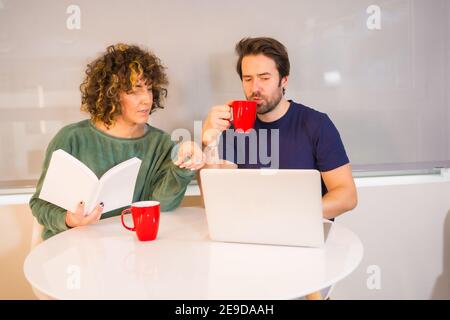 Nahaufnahme einer Frau mit einem Buch in der Hand Mit ihrem Freund über die Arbeit am Laptop diskutieren Stockfoto