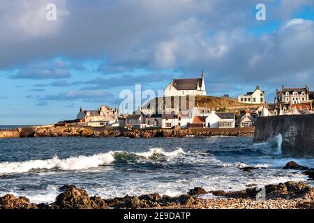 FINDOCHTY MORAY COAST SCHOTTLAND KIESSTRAND KRACHENDE WELLEN UND EIN WEISSE KIRCHE ODER KIRK AUF DEM HÜGEL Stockfoto