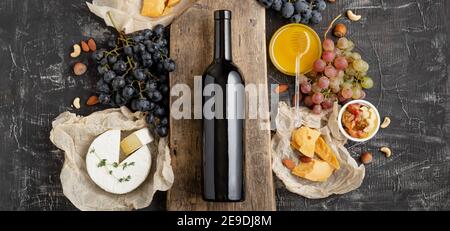 Rotwein-Flasche an Bord, Weingetränk Mockup. Rahmen aus Gastronomie verschiedene Käse Trauben Honig Nüsse. Abendessen im Restaurant, Weinprobe Gourmet Stockfoto