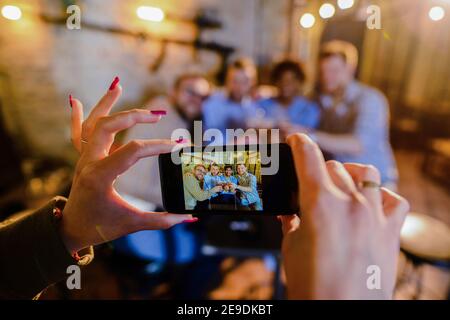 Nahaufnahme von weiblichen Händen, die ein Bild von vier glücklichen männlichen Freunden machen, die in einer Bar trinken. Stockfoto