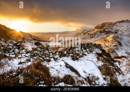 Wunderschöner Lake District Sonnenaufgang, wenn die Sonne über dem Horizont aufgeht. Im Vordergrund ist eine alte Steinmauer zu sehen. Stockfoto