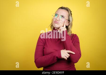 Junge kaukasische Frau trägt lässiges rotes T-Shirt auf gelbem Hintergrund ernstes Gesicht Denken über Frage mit Hand auf Kinn, nachdenklich über confu Stockfoto