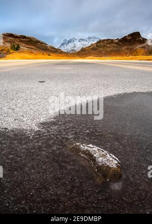 Die schneebedeckten Langdale Pikes von einem gefrorenen Blea Tarn mit goldenem Morgenlicht gesehen. Lake District, Großbritannien. Stockfoto