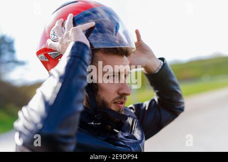 Junger sportlicher Mann, der Motorrad-Helm auf den Kopf stellt. Bereit für eine Fahrt. Stockfoto