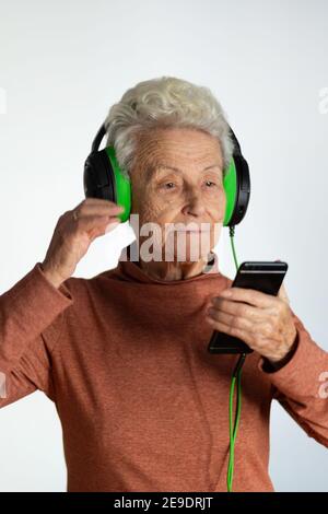 Ältere Frau, die Musik mit Kopfhörern und Smartphone hört. Blick auf Handy-Bildschirm mit Handy-Player-App Online-Musik hören, lernen foreig Stockfoto