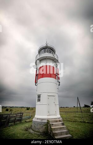 Kleiner Leuchtturm auf einem grünen Feld bei bewölktem Wetter mit Treppenstufen bis zu einer Tür Stockfoto