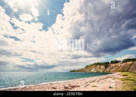 Strand mit Klippen an einer skandinavischen Küste im Sommer. Sonne scheint durch die Wolken über einer dänischen Insel. Stockfoto