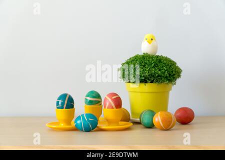 Osterdekoration mit bunt bemalten hausgemachten ostereiern mit modernem Muster auf gelben Untersetzern und Brunnenkresse im Topf auf Holztisch. Ostern zurück Stockfoto