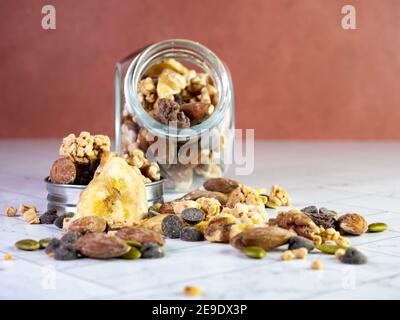 Glas mit Nüssen, Trail-Mix, Müsli, Bananenchips, getrocknete Früchte, Schokolade Chips, Mandeln, Erdnüsse, Walnüsse und Sonnenblumenkerne. Gesunde gute Kohlenhydrate Stockfoto