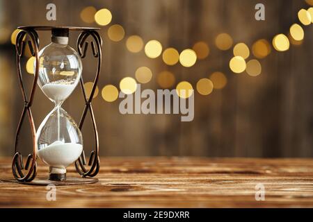 Sanduhr auf Holzschreibtisch gegen verschwommenes Licht Stockfoto