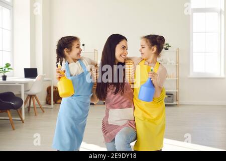 Glücklich lächelnde Mutter umarmt ihre zwei kleinen Zwillingstöchter, die ihr halfen, das Haus zu säubern. Stockfoto