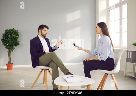 Frau mit Mikrofon in der Hand sitzt vor einem berühmten Mann und interviewt ihn. Stockfoto