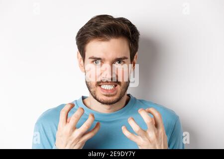 Nahaufnahme eines wütenden jungen Mannes mit Bart, schüttelnd Hände verrückt, quetschen Zähne und Stirnrunzeln wütend, stehend empört über weißen Hintergrund Stockfoto