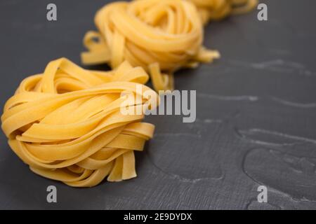 Reihe von hausgemachten Tagliatelle Nester, gelbe Pasta auf grauem Stein Hintergrund mit Kopierer Platz. Italienische Küche in den Farben des Jahres 2021. Frisch hausgemachtes oder Stockfoto