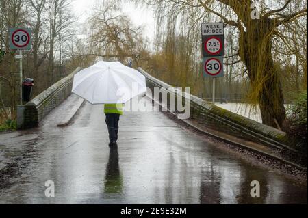 Sonning, Berkshire, Großbritannien. 4th. Februar 2021. Ein Mann mit einem riesigen Paresol geht über die Sonning Bridge. Nach heftigen Regenfällen in den letzten Tagen ist die Themse am Sonning in Berkshire in die Ufer geplatzt. Ein Hochwasser-Warnhinweis ist vorhanden und tief liegende Straßen, Wege und Felder sind überflutet. Obwohl die B478 über die Sonning Bridge wegen der Überschwemmungen geschlossen ist, ignorierten die Fahrer die Straßensperrschilder. Quelle: Maureen McLean/Alamy Live News Stockfoto