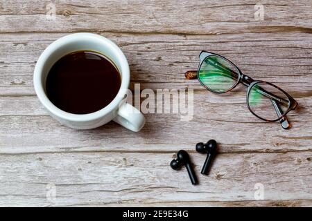 Schnurlose Ohrhörer auf einem Holztisch Oder Schreibtisch neben einem Kaffee und ein paar Gläser Stockfoto