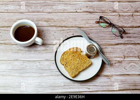 Toast und Marmelade auf einem Teller neben einem Kaffee Auf einem Holztisch, um die Frühstückszeit darzustellen Stockfoto